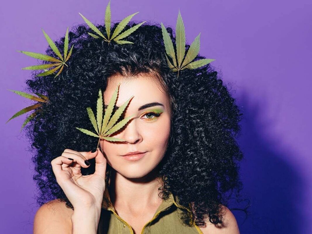 Woman holding marihuana leaf with purple background